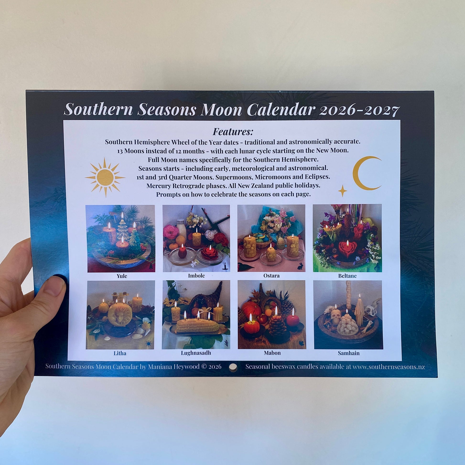A hand holds a printed Southern Hemisphere Moon Calendar back page showing a Sun and Moon with Calendar Features and a grid of colourful seasonal altars with beeswax candle collections labeled Yule, Imbolc, Ostara, Beltane, Litha, Lughnasadh, Mabon, and Samhain.