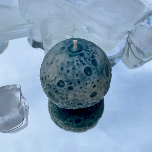 Spherical blue and white beeswax candle with textured surface to look like a realistic Moon on an icy blue and white mirror background