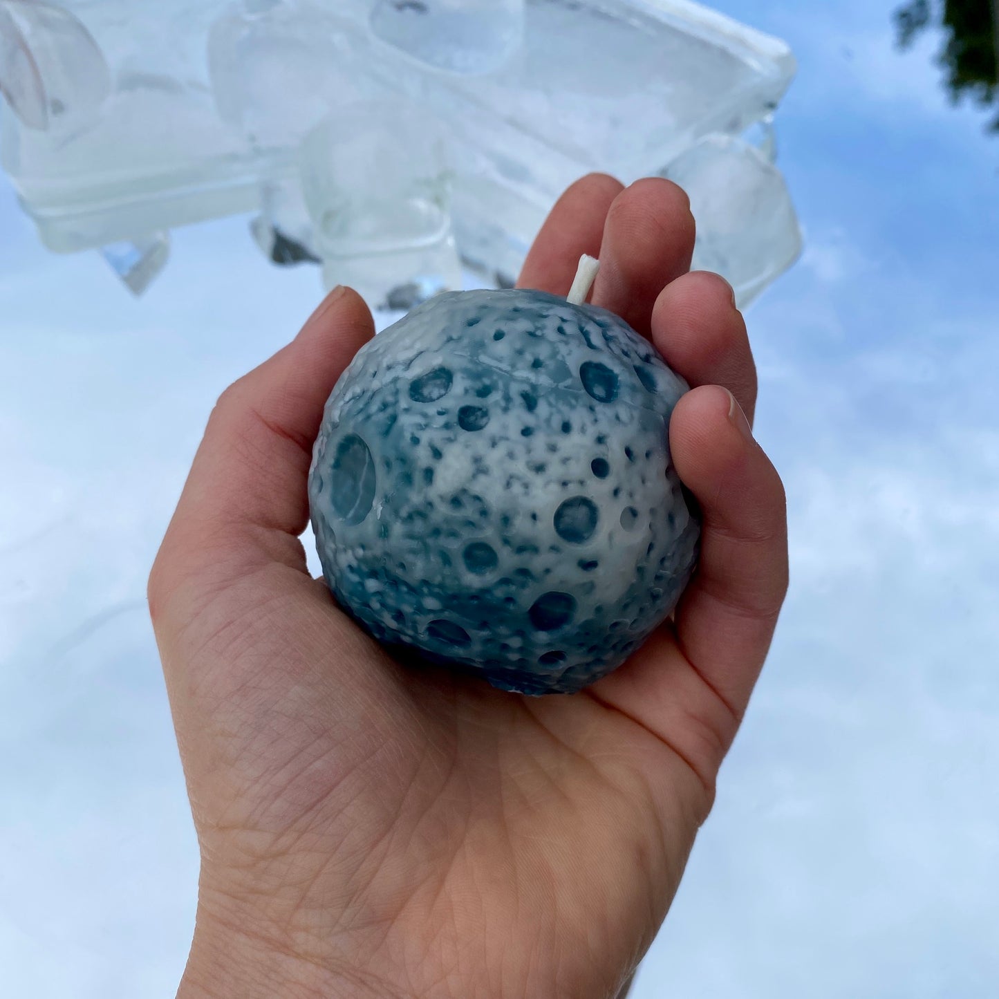 Hand holding a blue and white textured Moon shaped beeswax candle against an icy background